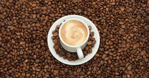 Keramische Tasse mit heißem, schwarzem Kaffee mit rotierendem Hintergrund aus frisch gerösteten Kaffeebohnen