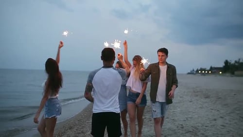 Friends Walking Dancing and Having Fun During Night Party at the Seaside with Bengal Sparkler Lights