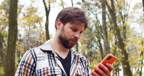 Man Uses Phone in Autumn Forest Setting