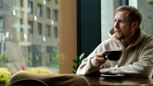 man drinking coffee in cafe by window overlooking city