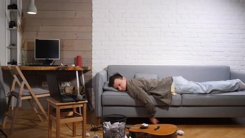 Young Man Lying on a Sofa Feeling Frustrated and Experiencing Writer's Block Surrounded By Crumpled