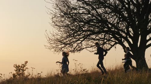Family Silhouetted Running up Hill at Sunset