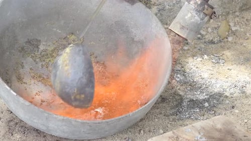 Molten lead in a metal bowl with ladle, industrial or crafting setting, close up