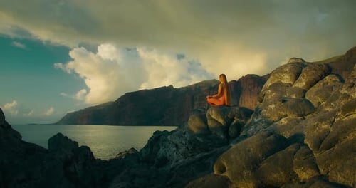 Belle fille aux cheveux longs pratiquant le yoga au bord de l'océan au coucher du soleil. Une femme médite en lotus positi