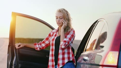 Woman Chatting on Phone by Car at Sunset