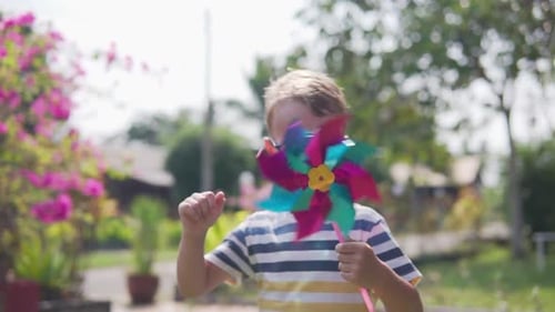 Boy in glasses is playing with pinwheel in a garden
