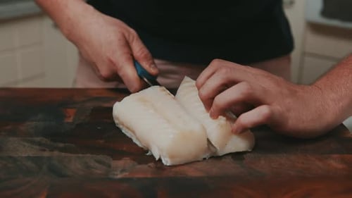 Man Cutting White Fish Fillet on Wooden Board