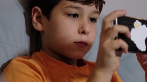 Boy Intently Playing on Mobile Phone Indoors