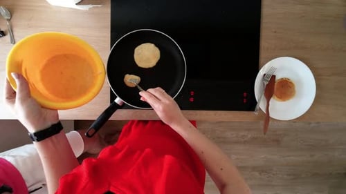 top down shot of female hands making pancakes on a hot black pan on electric stove