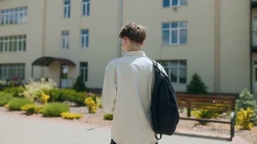 Rear View of Young Student with Backpack Arriving at a Modern School