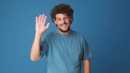 Happy man waving palm in greeting gesture isolated on blue background in studio