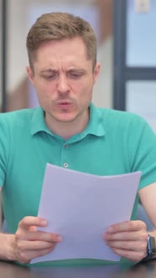 Man Reads Documents While Sitting at Desk Indoors