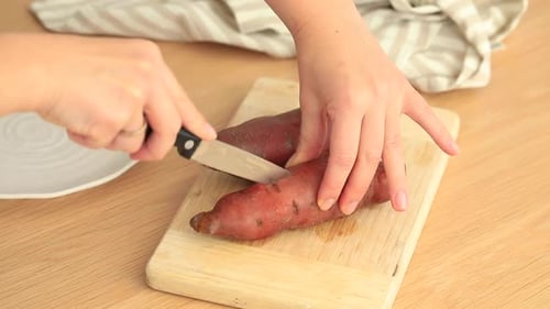 Cutting Raw Sweet Potatoes With Knife on Board