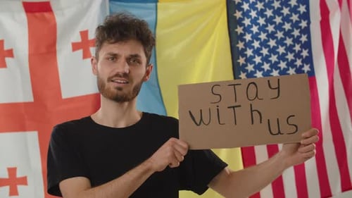 Man Holding Sign in Front of Flags