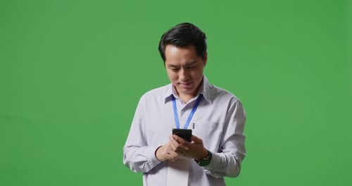 An Asian Business Man Using Mobile Phone An Looking Around On Green Screen Background In The Studio