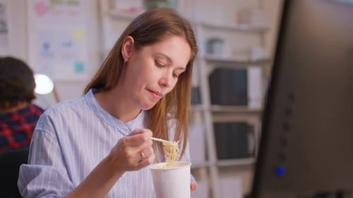 Caucasian businesswoman eatting noodles while work in office at night.