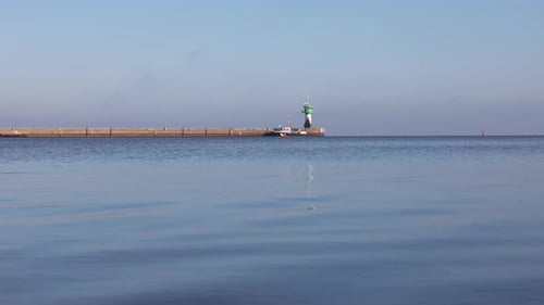 Peaceful seaside view in Luebeck-Travemuende with a long pier, green lighthouse, and calm blue