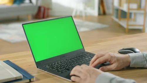 Professional Freelancer Works on a Laptop with Green Mock-up Screen while Sitting at the Desk in Hi