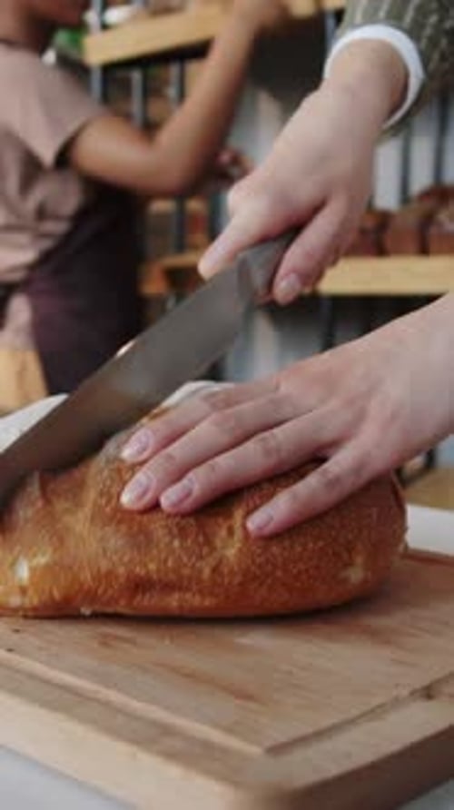 Close Up of Female Hands Cutting Fresh Loaf of Bread in Bakery