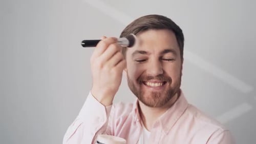 Smiling Man Applies Makeup with Brush