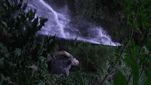 Rear view of male traveler standing in front of waterfall.