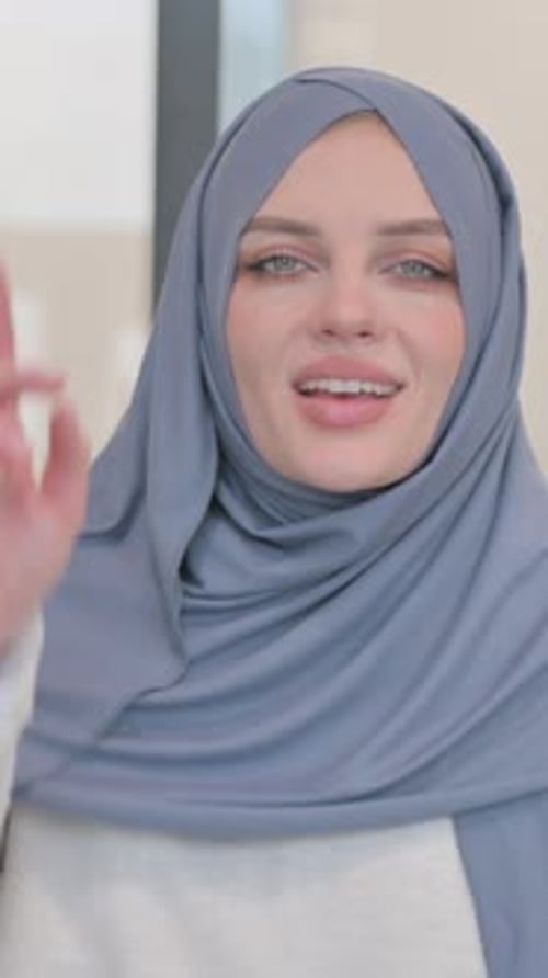 Smiling Woman in Hijab Pointing Upward Indoors