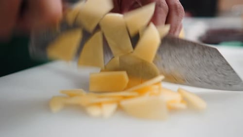 Closeup of a Professional Chef Quickly Cutting a Potato with a Sharp Knife in a Kitchen