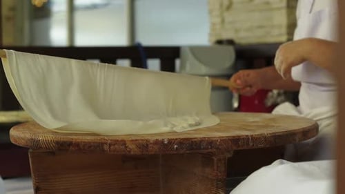 Frau rollt Teig mit Nudelholz auf einem Holztisch. türkisches Gebäck.