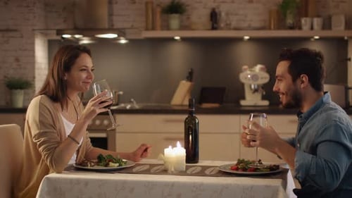Schönes Paar beim Abendessen bei Kerzenschein in der Küche. Sie trinken Wein, essen und reden. Beide sind