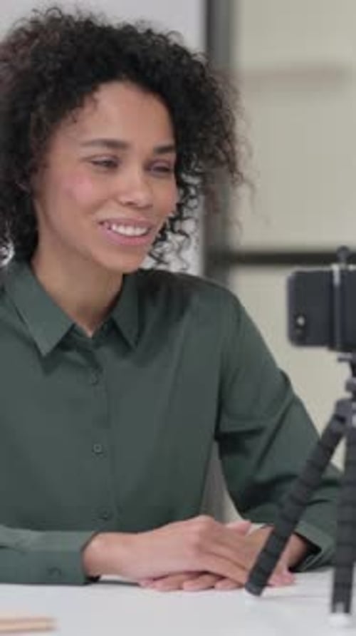 Woman Speaking to Camera at Desk Indoors