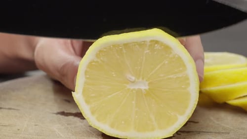 Cutting a piece of lemon on board with a large knife. Close up
