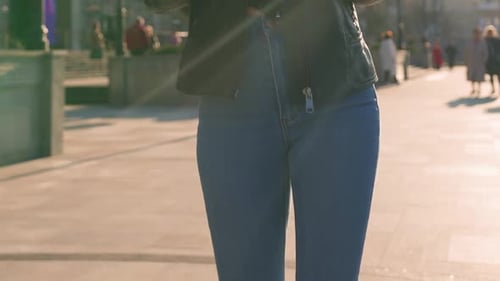 Slim Woman in Jeans Walking Through a City Park During Sunset