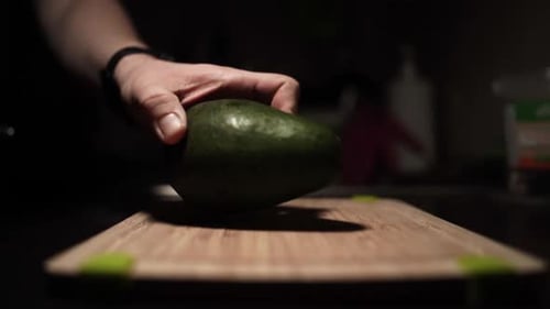 Person cutting green avocado on wooden cutting board