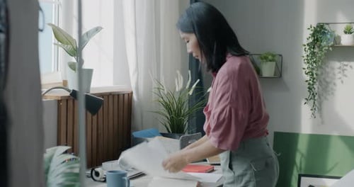 Fröhliche asiatische Frau, die den Schreibtisch aufräumt und Papier und Schreibwaren weglegt, konzentriert auf das Aufräumen in