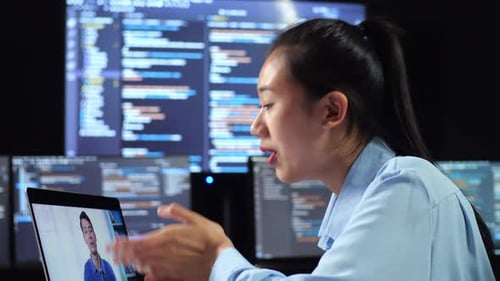 Side View Of Female Programmer Having A Meeting By A Laptop While Writing Code On Multiple Monitors