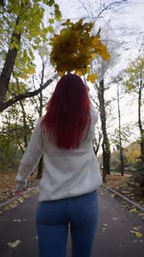 Mulher feliz caminha com um guarda-chuva do qual as folhas de outono estão voando