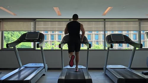 Fit Sporty Male Runner Running on Treadmill at Health Club - back view