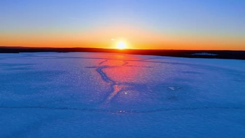 Sun setting over a vast frozen lake in winter landscape. Wide angle view of a frozen lake