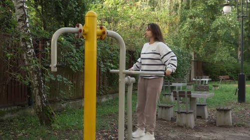 Woman Exercising on Outdoor Swaying Platform Machine for Leg Fitness in Park