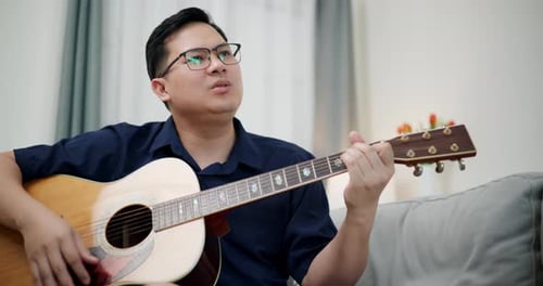 Man Plays Guitar on Gray Couch
