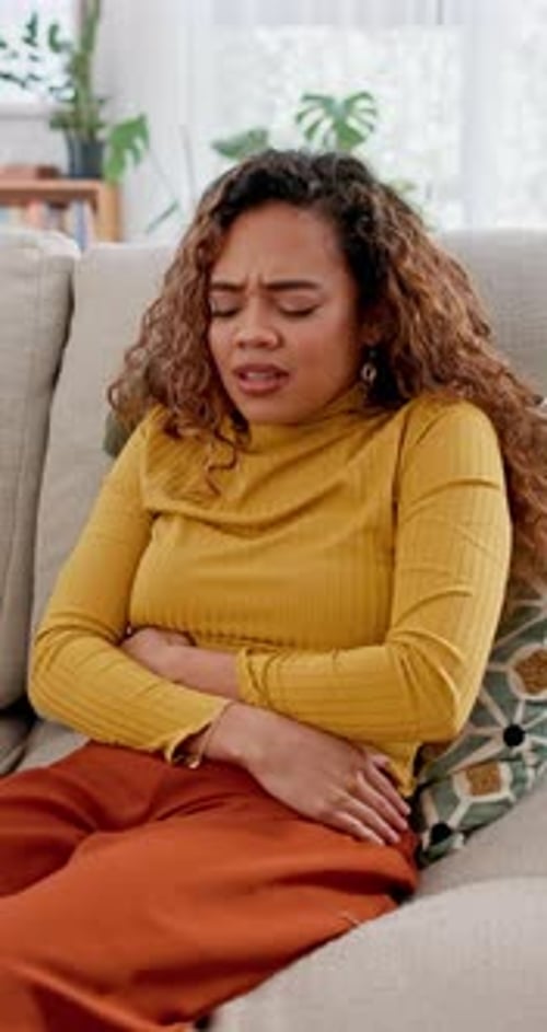 Stomach, ache and pain with woman on sofa for ibs symptoms, digestive issue and bloating
