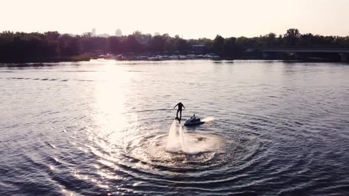Un jeune homme fait du flyboard près de la jetée et s'entraîne avec un Drone au coucher du soleil
