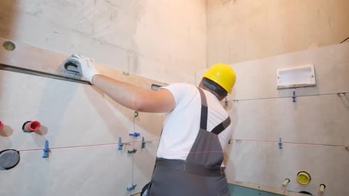 A Builder in Overalls is Installing Ceramic Tiles in a Bathroom Repair in a New Building