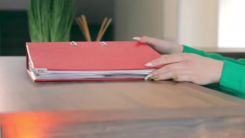 Hands pick up red binder on wooden desk