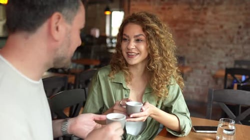 Beautiful woman with curly hair smiles while talking and drinking coffee with her partner in a cafe
