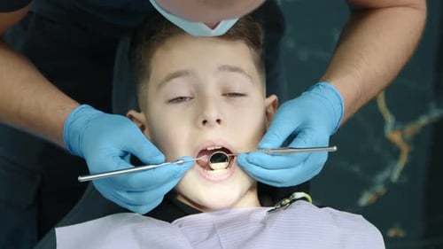Close Up of Kid Sitting in Dentist Chair Male Dentist Examines Teeth Gently