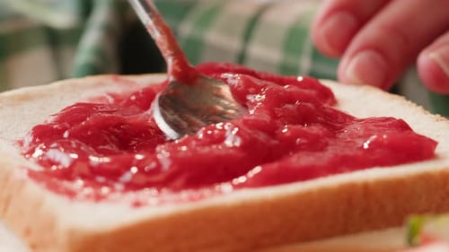 Cozinhando o tradicional café da manhã americano: pão fresco com geléia de frutas vermelhas, geléia doce vermelha pinga no pão