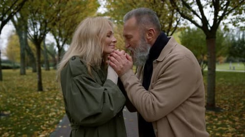 Happy adult couple kissing hands in romantic autumn atmosphere in fall park