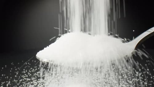 Pure white sugar cascades delicately into a spoon.