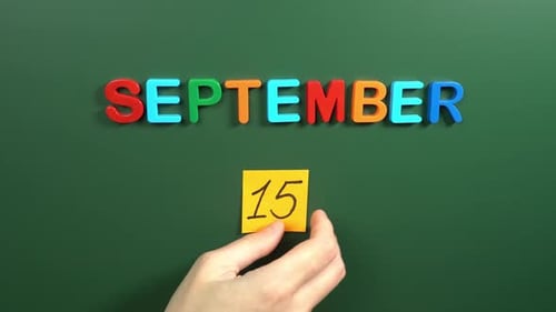 Hand sticking a sticker 15 September calendar day on school board. 15 date of September. Fifteenth